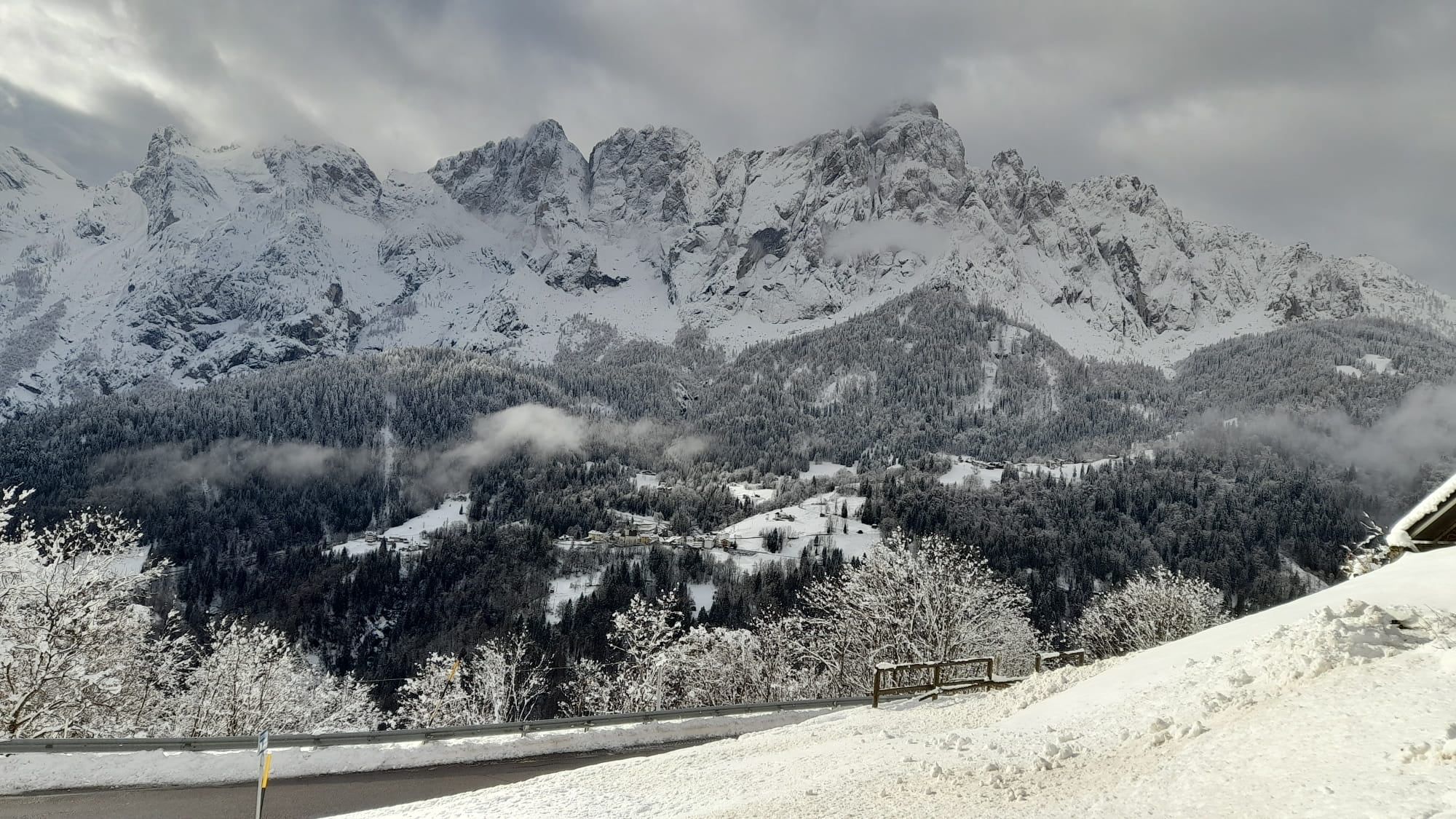 Le Dolomiti innevate viste da Pongan, con i boschi e le case della valle